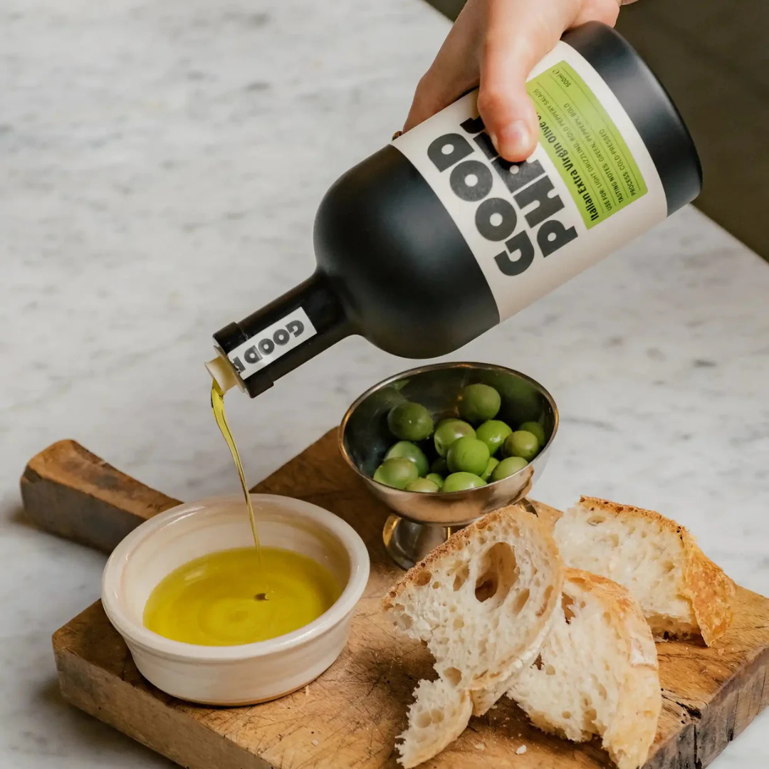 GOOD PHATS Italian Extra Virgin Olive Oil being poured into a dipping bowl with green olives and rustic bread